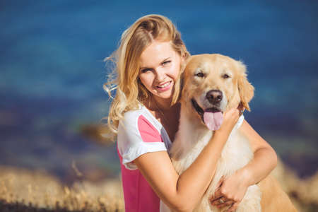 Portrait of beautiful woman with her retreiver dog playing near blue seaの写真素材