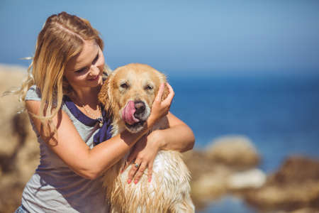 Portrait of beautiful woman with her retreiver dog playing near blue seaの写真素材