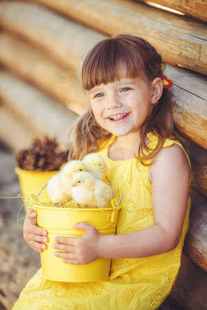 Happy little girl with a basket of small chickens sitting outdoorの写真素材