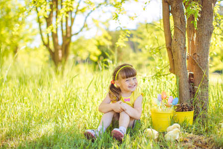 Happy little girl with a basket of small chickens sitting outdoorの写真素材