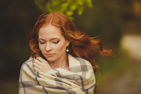 Portrait of young beautiful redhair woman standing in green summer parkの写真素材
