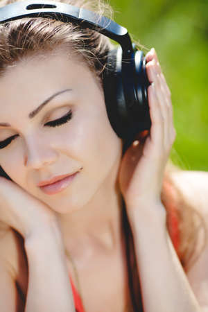 Close portrait of young beautiful smiling woman in headphones outdoors in summerの写真素材