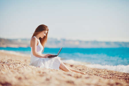 Cute woman with white laptop on the summer beachの写真素材
