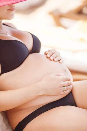 Pregnant beautiful woman in swimming suit on the beach outdoorsの写真素材