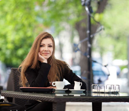 Portrait of young beautiful woman sitting in a cafe outdoor drinking coffeeの写真素材
