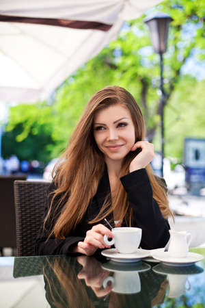 Portrait of young beautiful woman sitting in a cafe outdoor drinking coffeeの写真素材