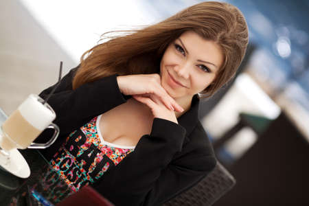 pretty smiling young woman sitting in the cafe with a cup of coffeeの写真素材