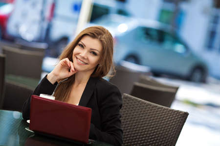Portrait of beautiful woman in winning pose and smiling sitting in a cafe with laptop outdoorの写真素材
