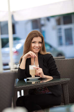 pretty smiling young woman sitting in the cafe with a cup of coffeeの写真素材