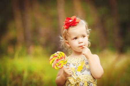 happy little girl licks sweet candy nature summer outdoorの写真素材