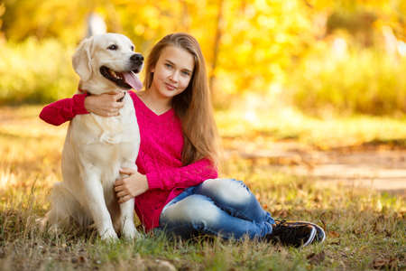 portrait of Smiling young girl posing with a labrador retriever dog out in autumn beautiful parkの写真素材