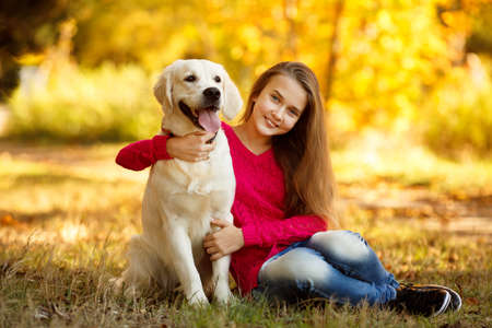 portrait of Smiling young girl posing with a labrador retriever dog out in autumn beautiful parkの写真素材