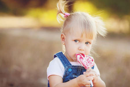 cute little girl eating a lollipop on the grass in summertimeの写真素材