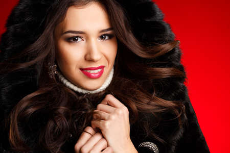 portrait of Young woman in black furry hood on red background  Studioの写真素材