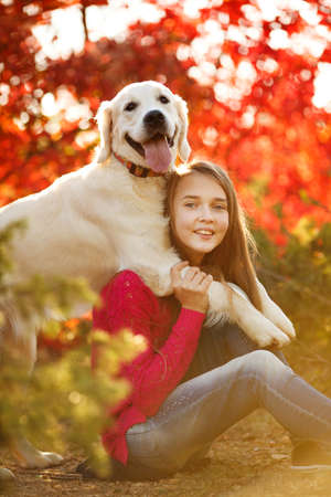 portrait of Smiling young girl posing with a labrador retriever dog out in autumn beautiful park