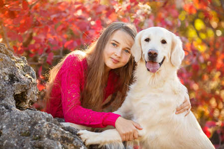 portrait of Smiling young girl posing with a labrador retriever dog out in autumn beautiful park