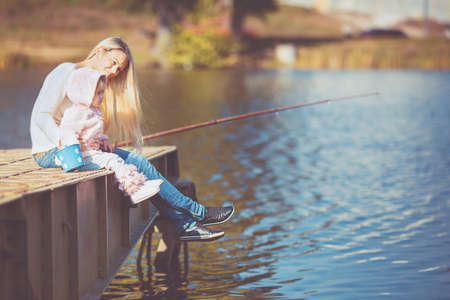 Woman with little daughter sitting near water turned backの写真素材