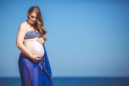 Happy beautiful young pregnant woman at the seaside  Blue water and sky の写真素材