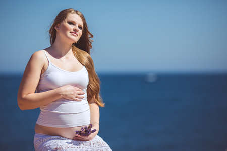 Portrait of happy beautiful pregnant woman over the sea  Blue water and sky behind 