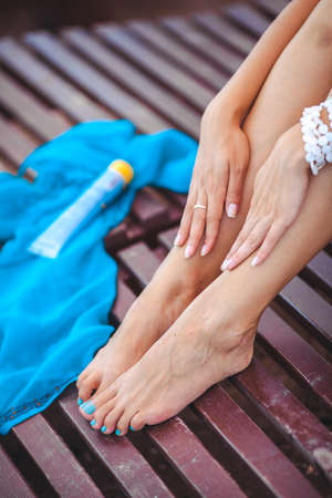 Tan woman applying sun protection lotion on her legsの写真素材
