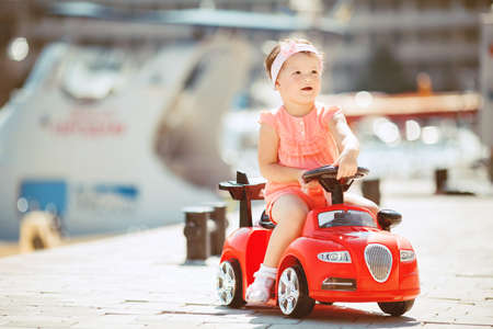 Cute little girl playing with a red car on the beach in the summer outdoorsの写真素材