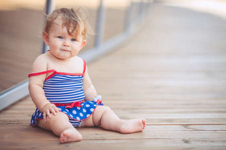 portrait of a little adorable infant girl sitting on the floor in summer park outdoorsの写真素材