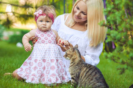 Young mother with child and a cat having fun on green lawn on summer dayの写真素材