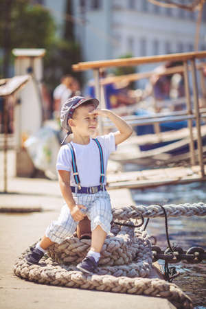 Cute little sailor boy having fan near boats on pier near the sea  Outdoor の写真素材