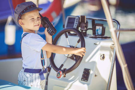 Cute little sailor boy having fan near boats on pier near the sea  Outdoor 