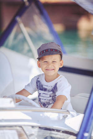 Cute little sailor boy having fan near boats on pier near the sea  Outdoor の写真素材