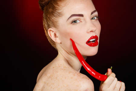 portrait of Beautiful redhair topless woman with red chili pepper in her hand  Isolated on black beckground  Bright makeup and red lips の写真素材