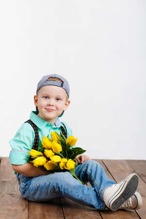 Smiling boy holding a bouquet of yellow tulips in hands sitting on wooden floorの写真素材