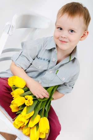 portrait of a smiling guy with a bouquet of yellow tulips flowers in hand sitting on a chair near...