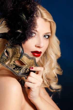 close-up portrait of beautiful blonde woman with bright make up hiding venetian carnival mask on dark の写真素材