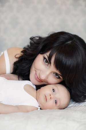 portrait of Young happy mother with her newborn baby lying on bed in home interior
