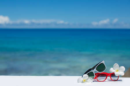 Two pair of sun glasses on a beach table on blue ocean backgroundの写真素材