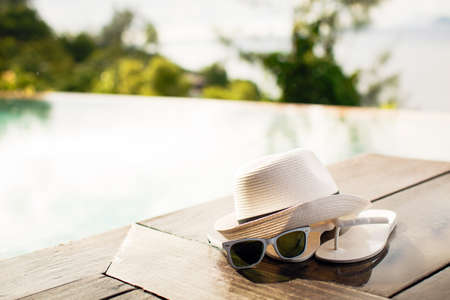 Pair of white flip flops by the pool on a bright blue, green, purple and white striped towel with sunglasses and big white floppy hatの写真素材