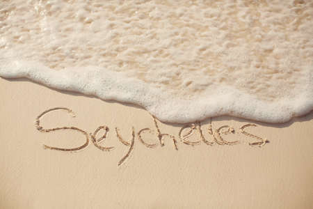 water surf edge on beach sand with seychelles inscriptionの写真素材