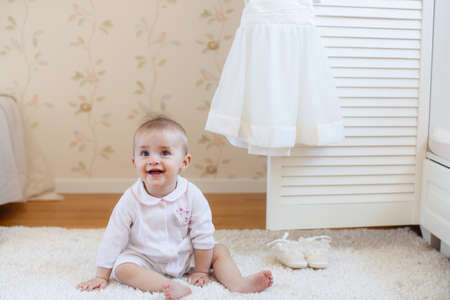 Adorable baby girl with curly hair wearing a dress playing on the floorの写真素材
