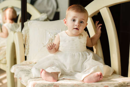 Adorable baby girl with curly hair wearing a dress playing on the floorの写真素材