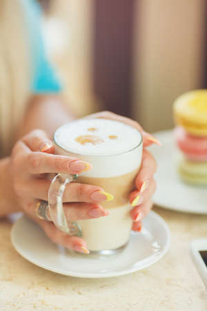 Cup of hot latte coffee with colorful macaroon cookies standing on table at cafe or home  Female holding a cup of latte coffeeの写真素材