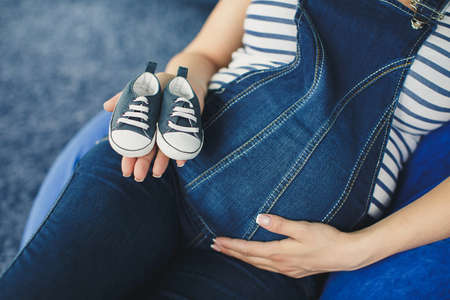 Pregnant woman in jeans knickers holding pair of small male shoes for baby  Shallow dof の写真素材
