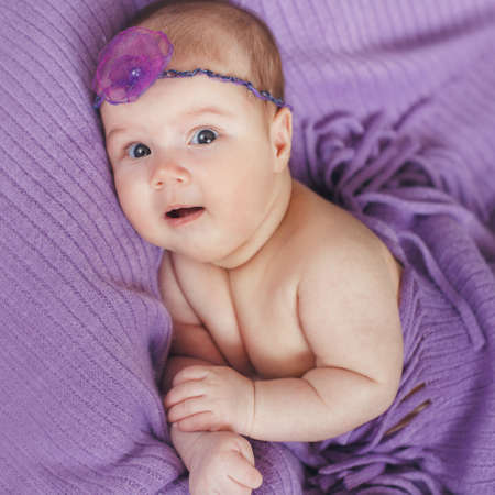 Caucasian baby boy covered with pink towel joyfully smiles at camera