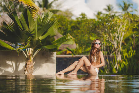 Shiny beautiful girl  Portrait of beautiful young women in bikini smiling on camera with a swimming pool on the backgroundの写真素材