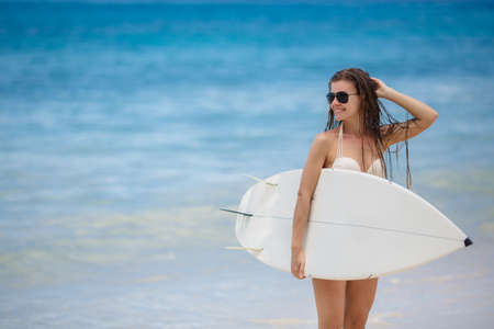 Beautiful Young Woman Surfer Girl in Bikini with Surfboard at a tropical Beachの写真素材