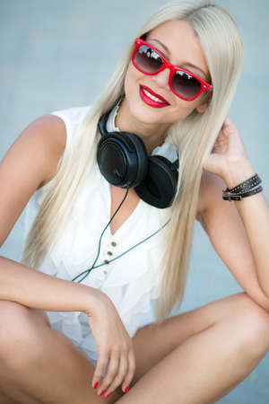 Portrait of a blonde girl with black sunglasses and headphones  closeup portrait of a sexy beautiful woman posing in headphones outdoorsの写真素材