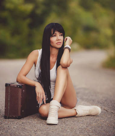 Traveler young girl in panties sits on the road with a suitcaseの写真素材