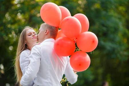 summer holidays, celebration and dating concept - couple with colorful balloons in the city. Young couple kissing among white columns and holding bunch of balloonsの写真素材