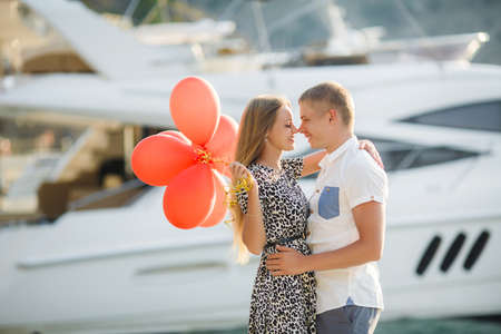 summer holidays, celebration and dating concept - couple with colorful balloons in the city. Young couple kissing among white columns and holding bunch of balloonsの写真素材