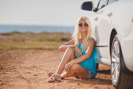 happy young woman with car - sexy rich lady driver with long blond healthy hair at automobile . spring - summer portrait . beautiful slim fashion girl posing near carの写真素材
